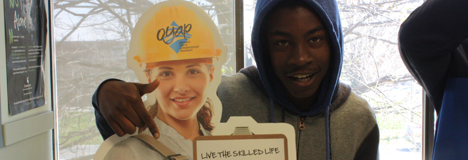 Male student standing beside Ontario Youth Apprenticeship Program cutout